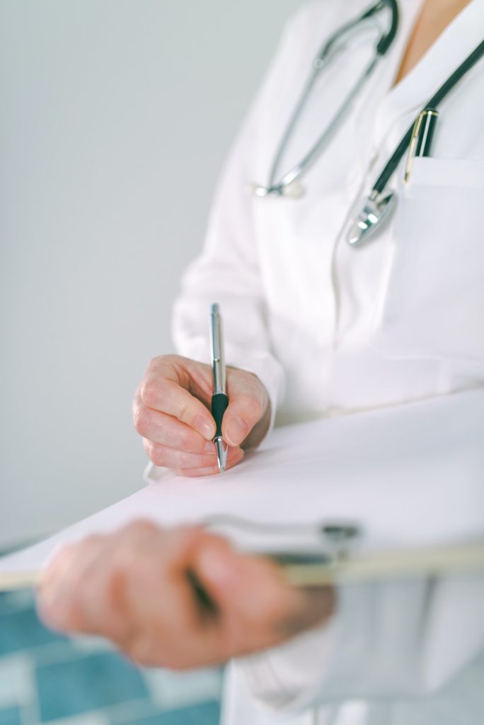 Female doctor in white uniform writing on clipboard paper