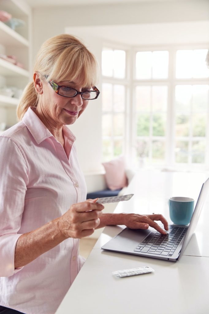 Mature Woman At Home Looking Up Information About Medication Online Using Laptop